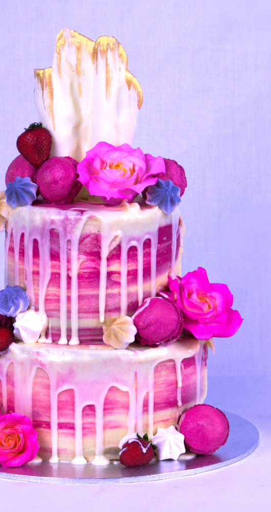 Pink two-tiered cake with an array of flowers and icing dripping over the sides